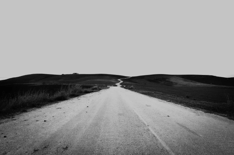 an empty road leading uphill in the middle of a grass and dirt field