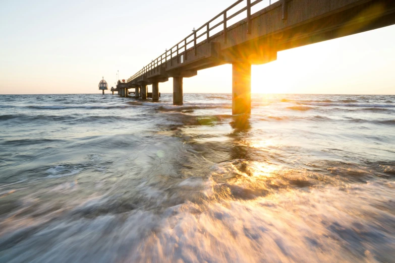 the sun is coming up behind an empty bridge in the ocean