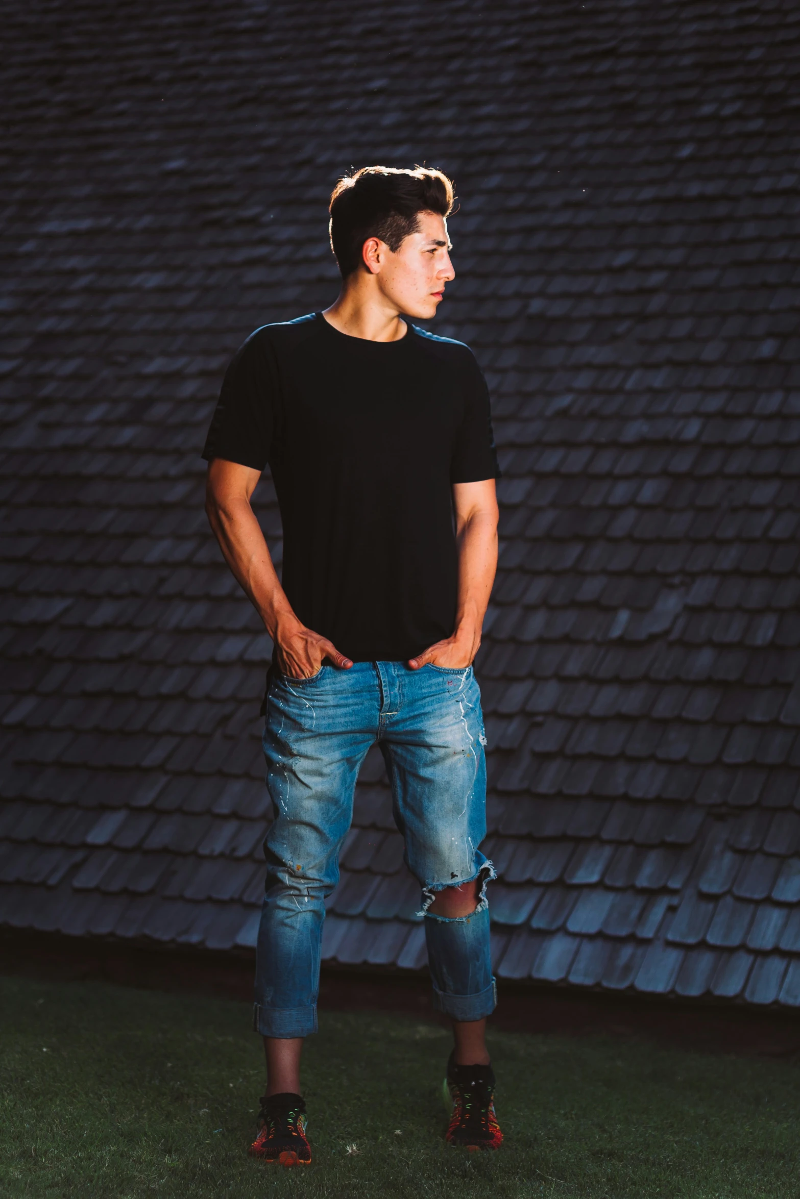 a male in ripped jeans stands against a background with a dark building