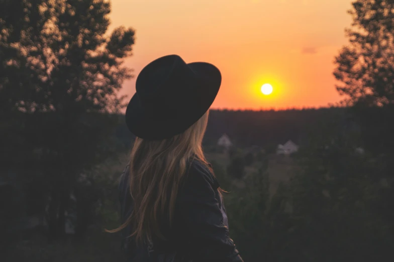 a woman is wearing a hat looking at the sun