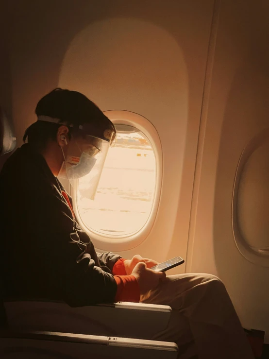 man in hat sitting inside airplane, using cellphone