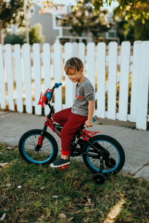 a small boy in striped pants on a little red bike