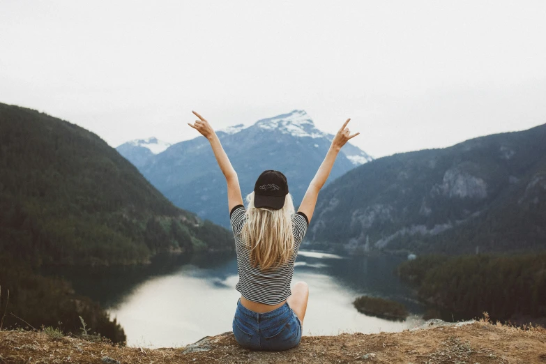 a woman sits on the edge of a cliff, and raises her arms up in the air