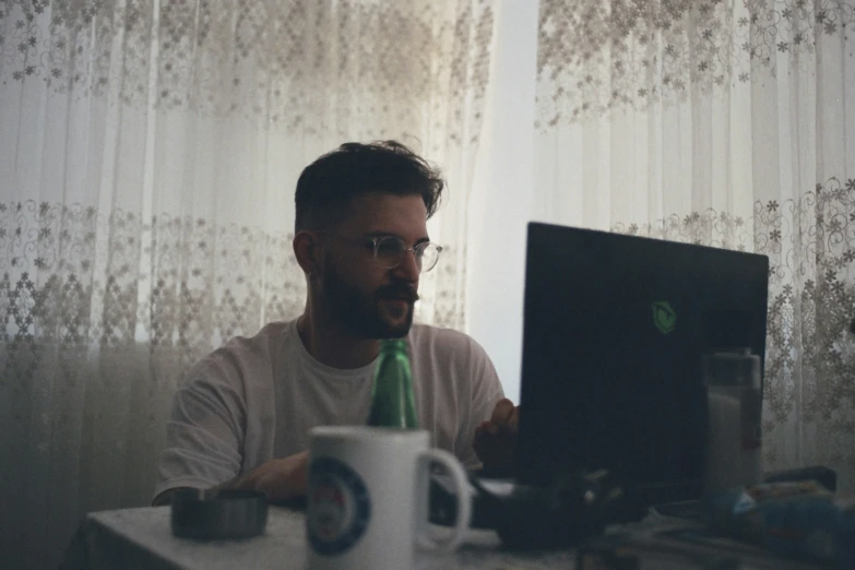 a man looking at a computer screen with a mug on the desk