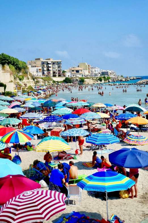 an outdoor beach has umbrellas, people and boats