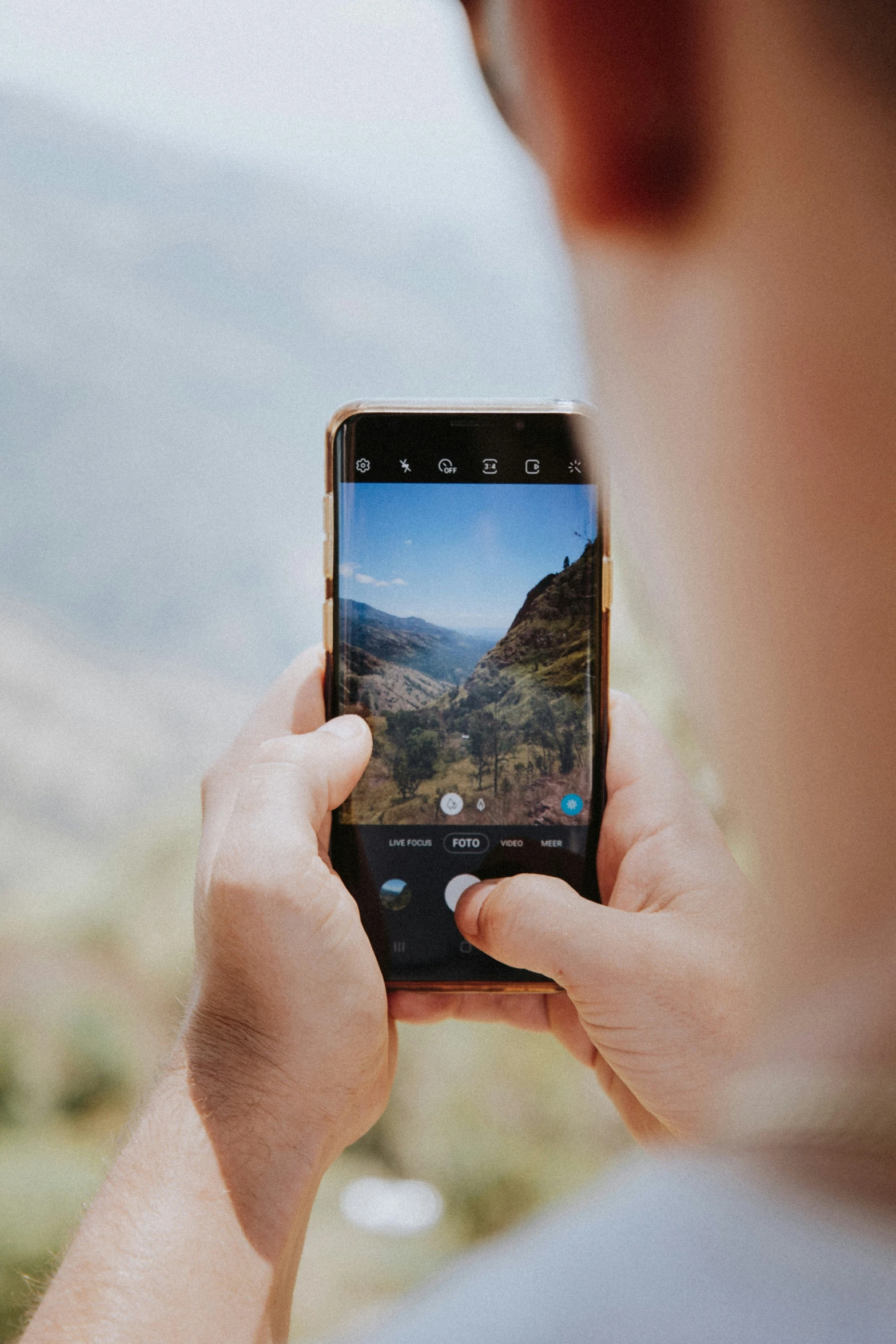 a person holding a cell phone while standing next to a mountain