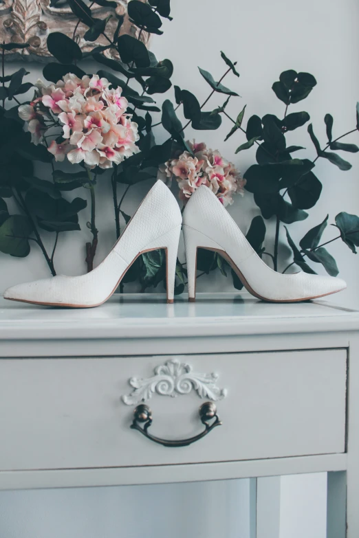 a pair of white high heeled shoes sitting on top of a white cabinet