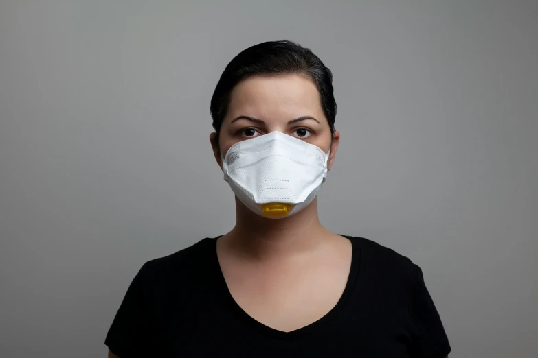a woman wearing a mask in front of a grey wall