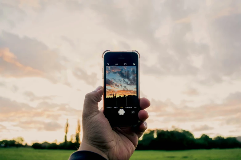 person taking po of sunset with cell phone