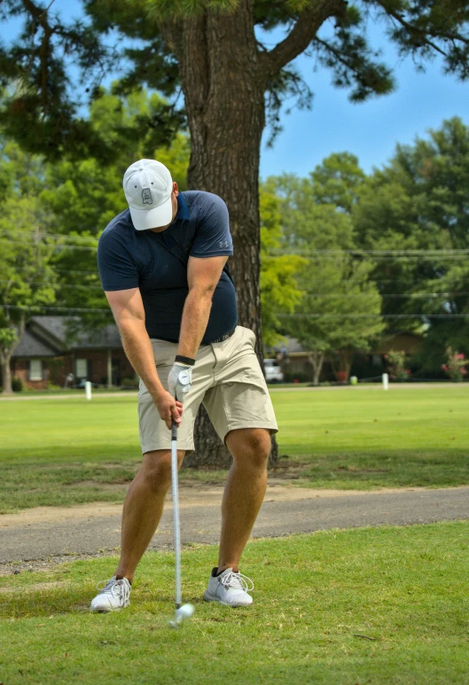 a man wearing a baseball cap and shorts stands leaning forward with a golf club