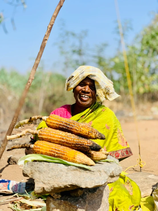 the woman is sitting on the rock near a bunch of corn