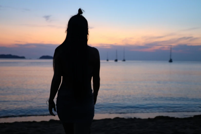 the silhouette of a woman standing in front of an ocean with sailboats in the distance