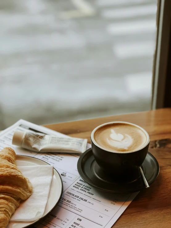 the croissant sits next to the coffee and newspaper on a table