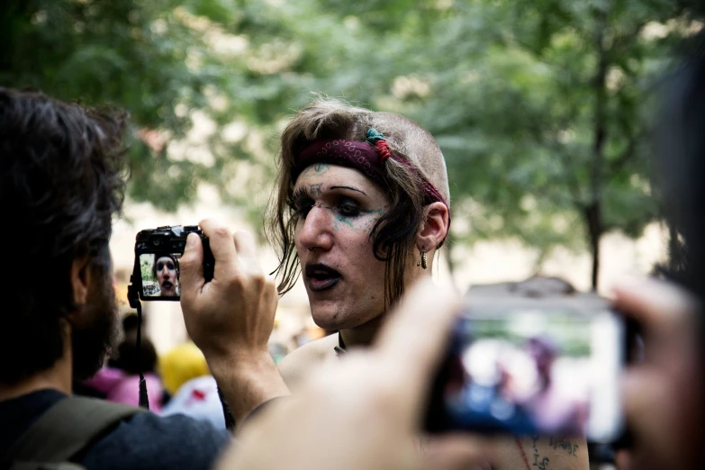 a man with painted face and neck has two cameras around his head