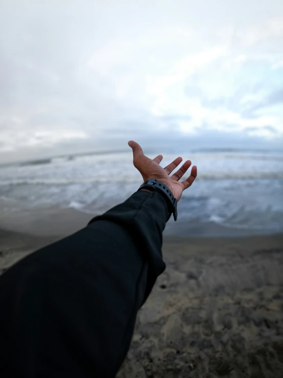 person standing on the beach with their hand out to see the ocean