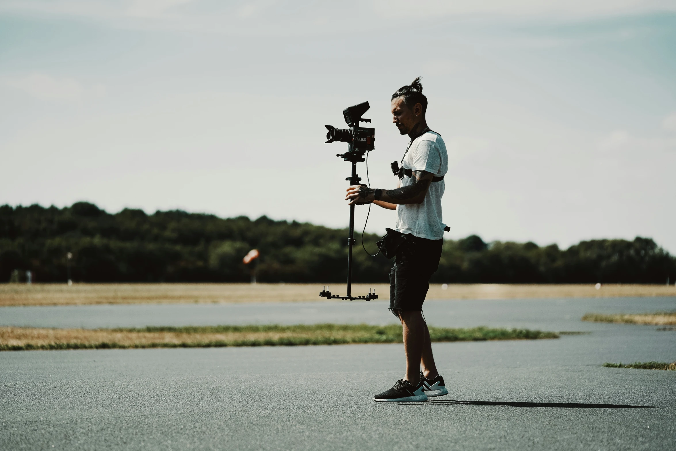 man with a camera standing on a road next to a lake