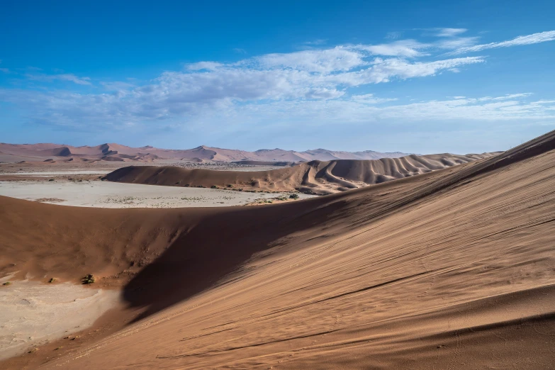 some sand hills and mountains under a cloudy sky