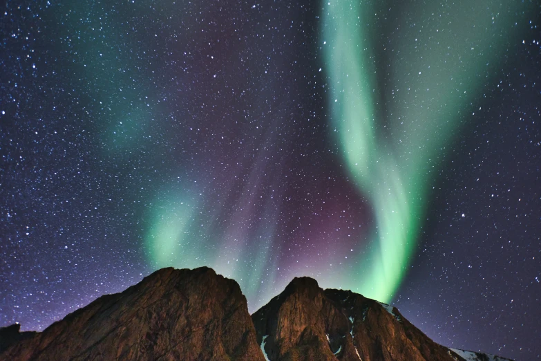 green and purple aurora lights against the sky above snowy mountains