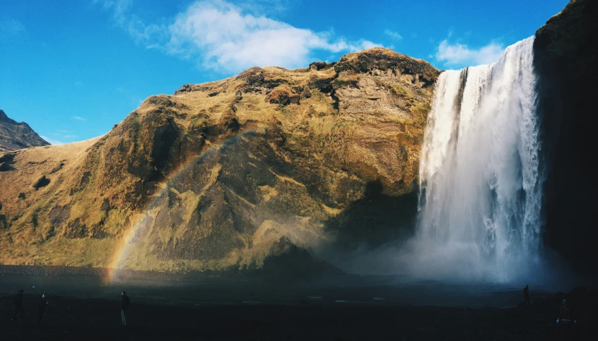 a rainbow falls out of a mountain in front of a waterfall