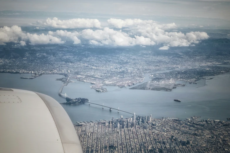 the wing of an airplane flying over a city with clouds