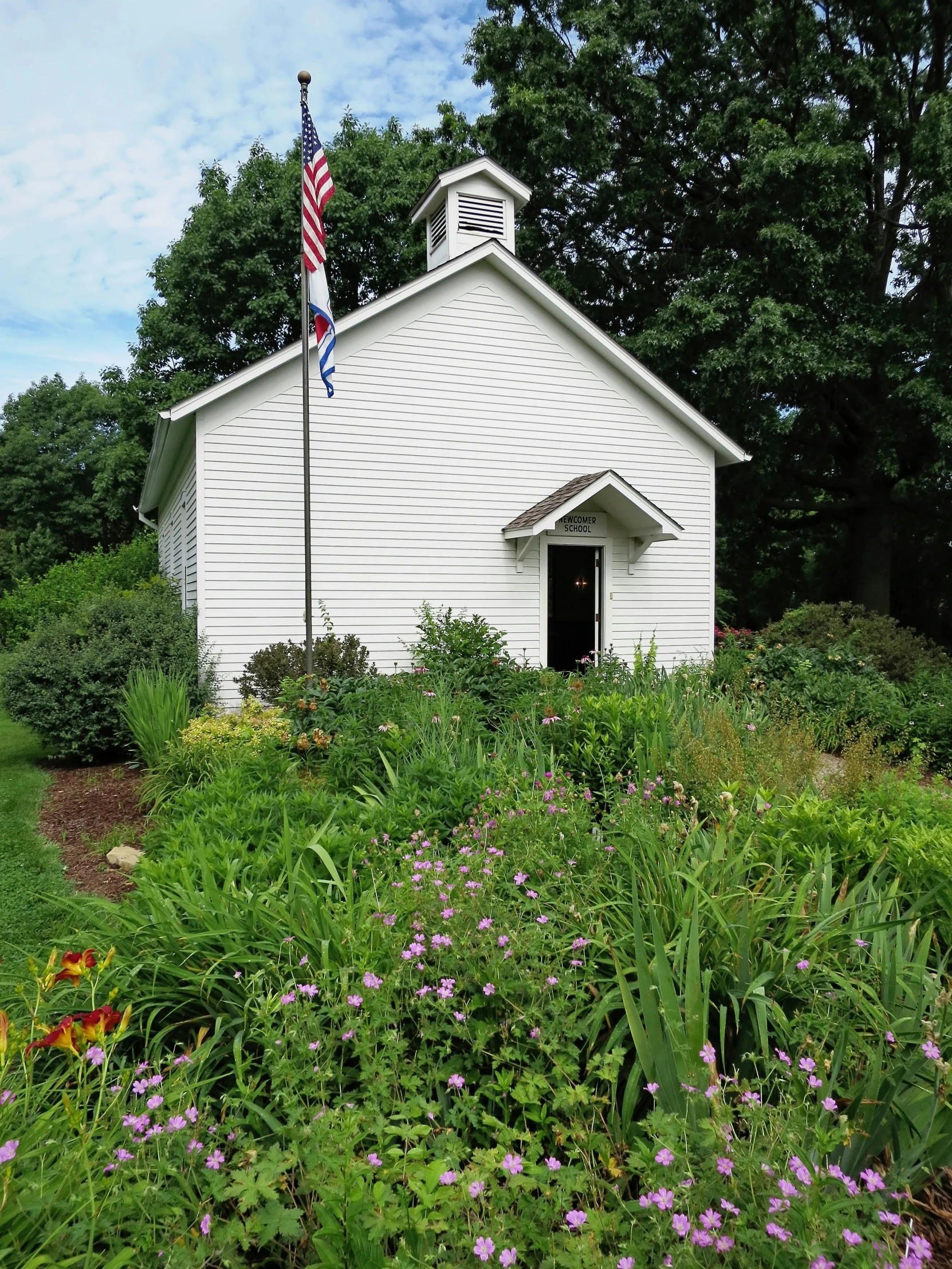 an old white church sits amongst the green and purple flowers