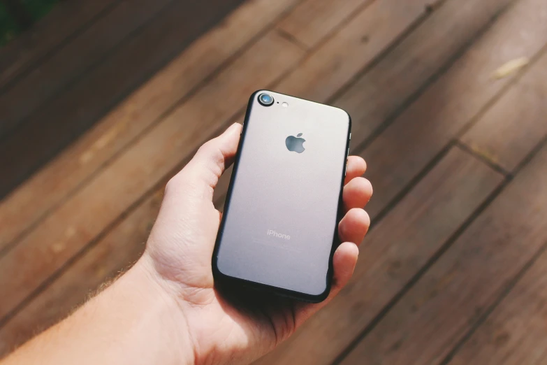 a hand holding a silver iphone over a wood floor