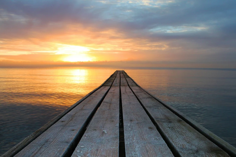 a wooden pier stretches out into the ocean as the sun sets