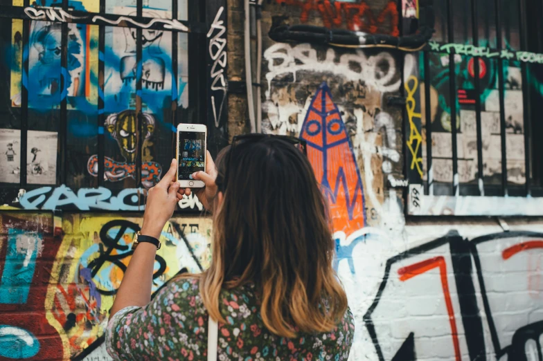 woman taking picture with her cellphone in front of wall of graffiti