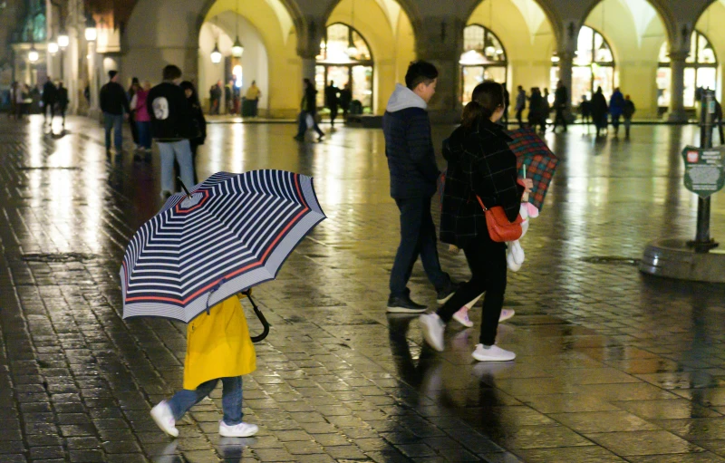 a group of people walking along a sidewalk holding umbrellas