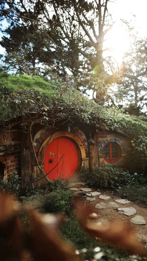 a red door in the side of a forest with green grass on top