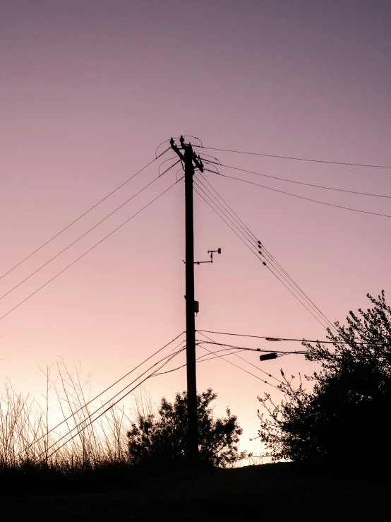 the silhouette of an electrical pole against a purple sky