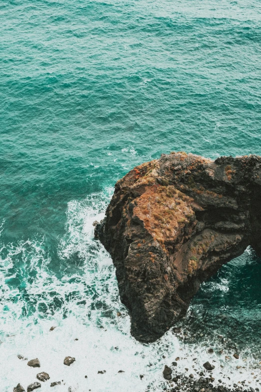 a couple stands next to a rock in the ocean