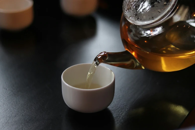 a cup being filled with liquid next to a tea kettle