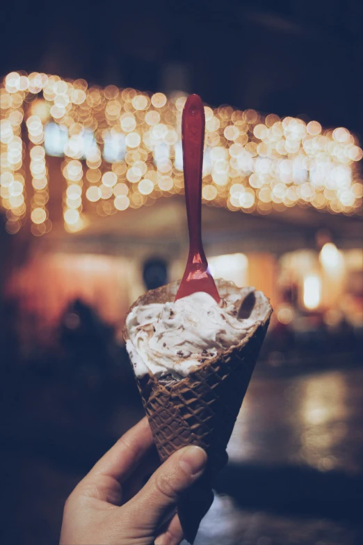 a hand is holding an ice cream cone with a spoon