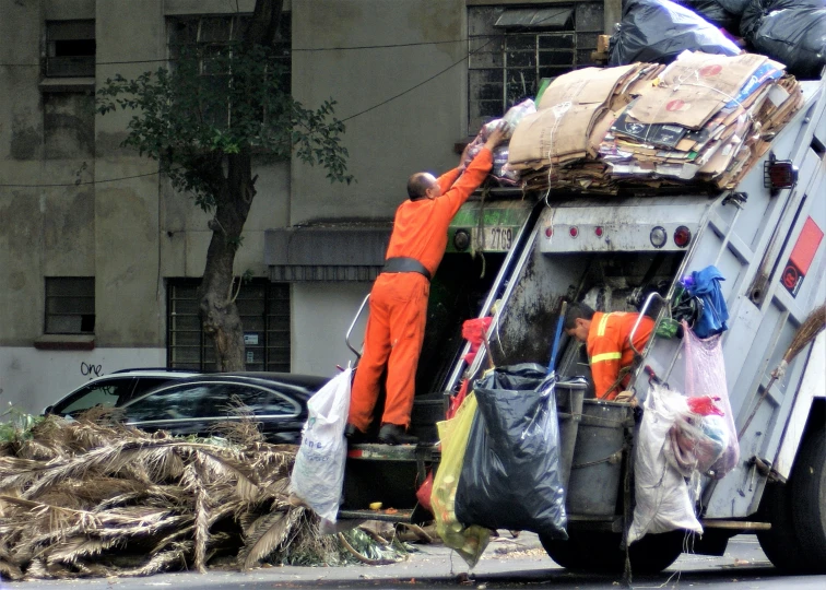 two men hing and unloading bags from a garbage truck