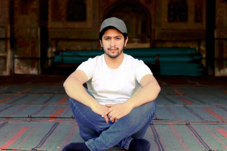 a man is sitting cross legged and wearing a hat