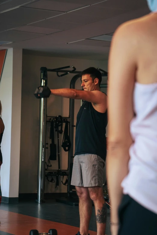 man with arms stretched out lifting weights and standing in front of woman