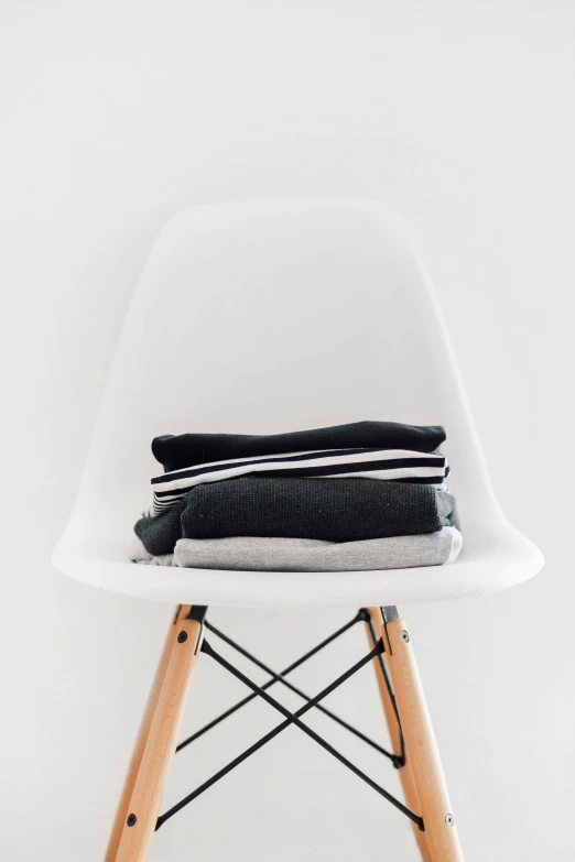 a stack of folded clothes sits atop a modern white chair
