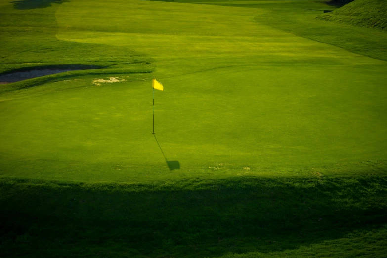 green golf field with yellow flag on the edge of it