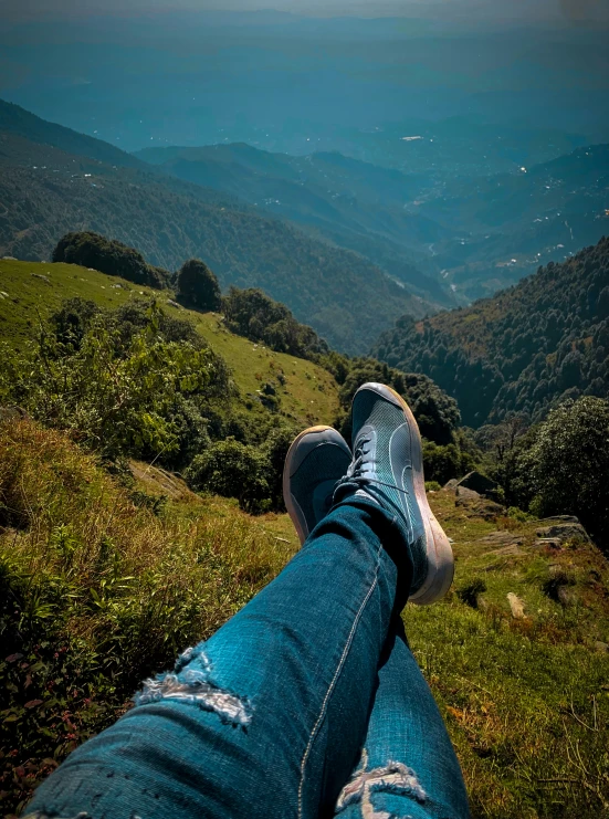 legs with ripped jeans and sneakers sitting on the top of a grassy hill