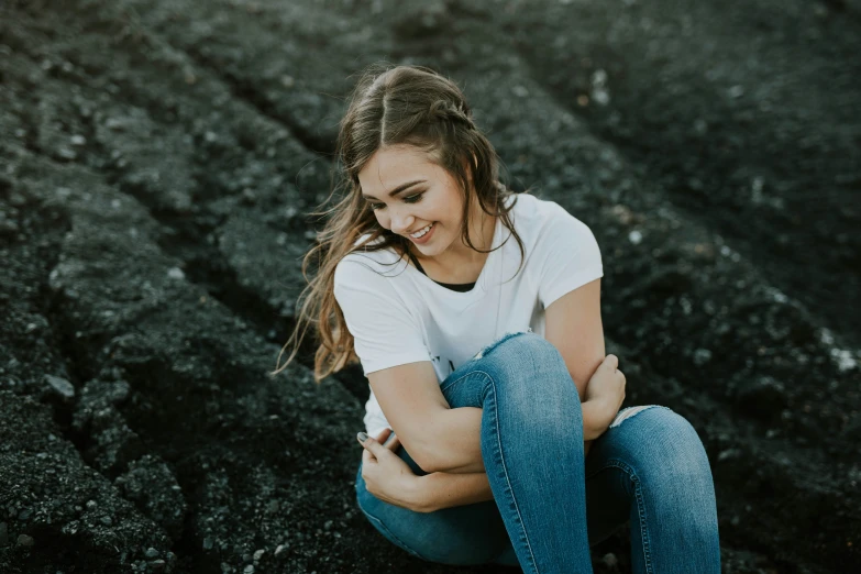 a young woman sits on a rock with her hands crossed