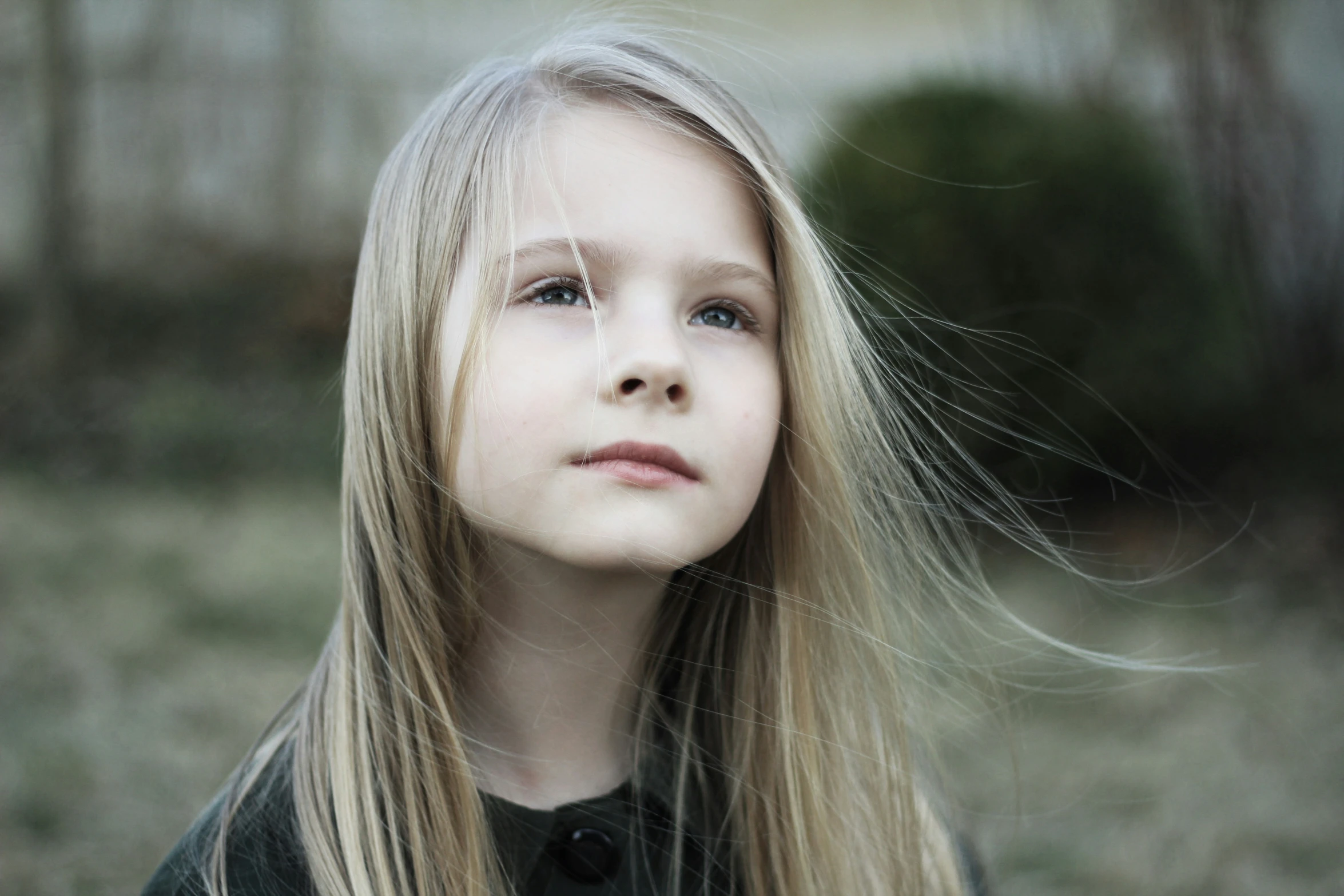 the young blonde girl is standing outside with long hair