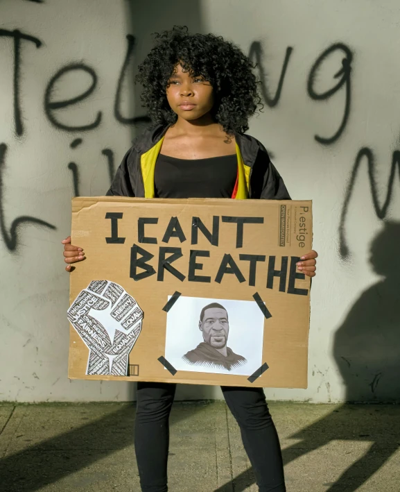 a woman holding a cardboard sign and a drawing of barack and i can't breathe