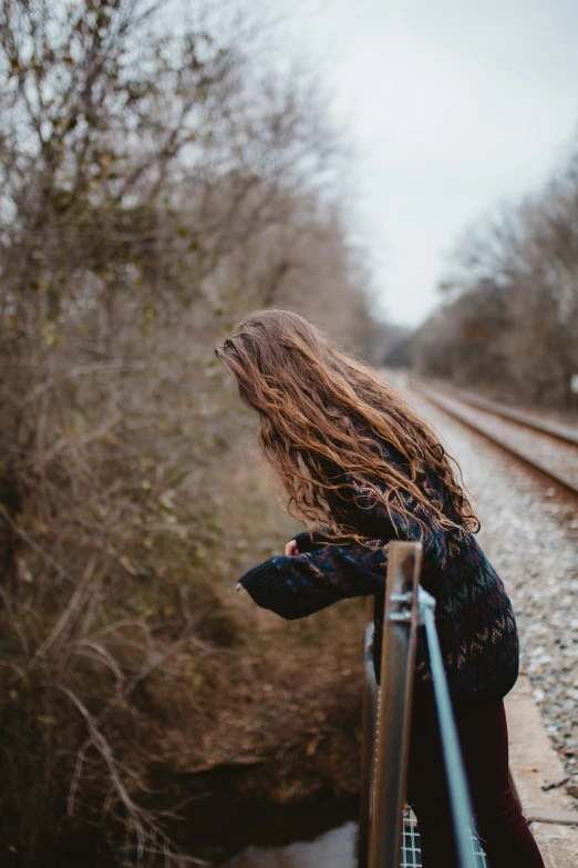 an attractive woman standing on train tracks looking back at the camera