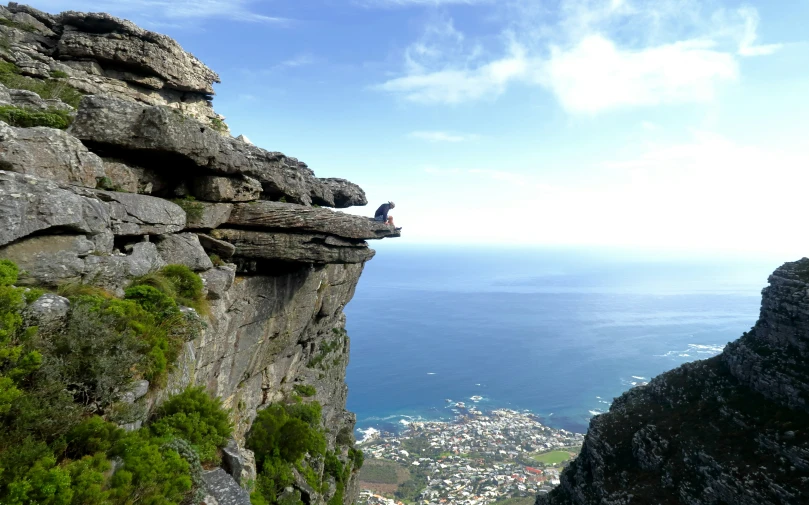 a man sits on the edge of a cliff overlooking the ocean