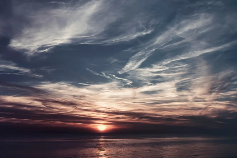 the sun setting behind some cloud formations over the ocean