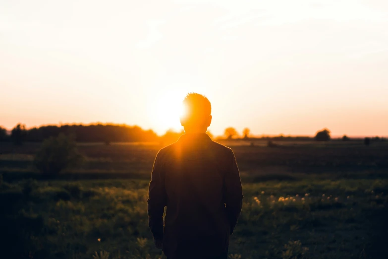 a man standing in a field with the sun shining through