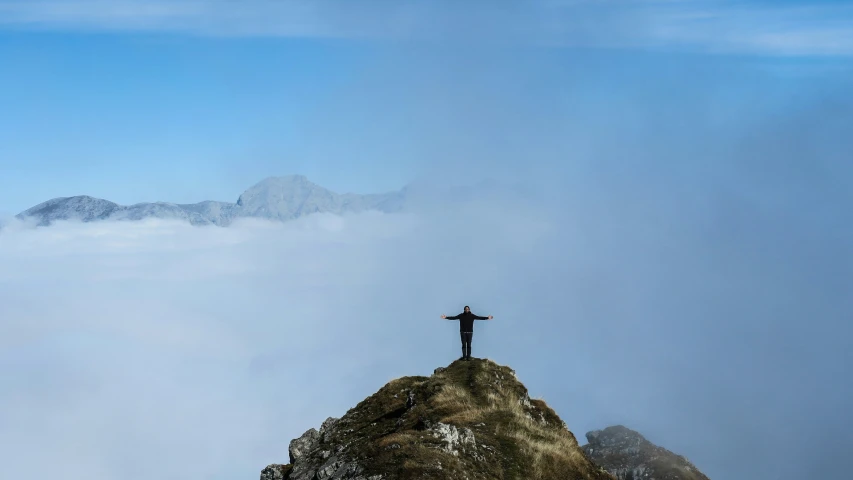 a man standing on top of a tall mountain with his arms outstretched