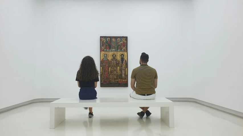 two people are sitting on the bench in front of the painting