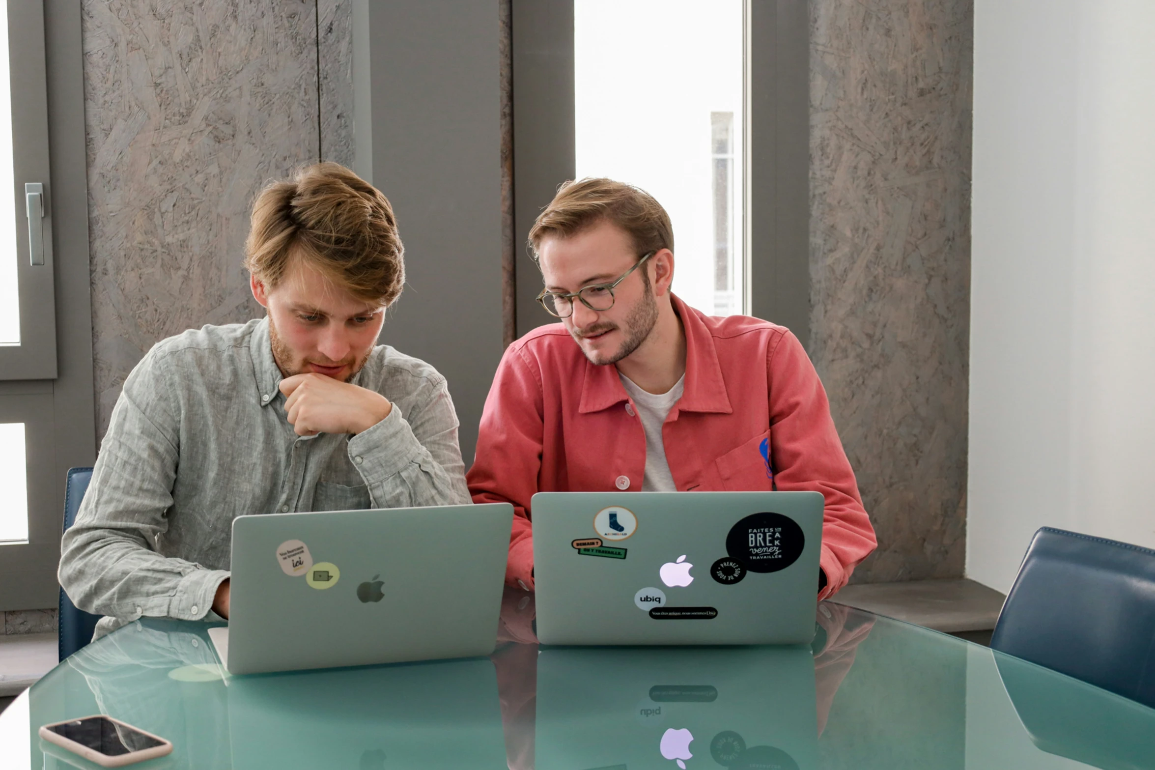 two people sitting at a table with two laptop computers